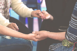 A close up of people holding hands while sitting in a circle. Learn more about the support Crossroads family counseling can offer by searching for an Anthem therapist near me, or a therapist in Arcadia, AZ.
