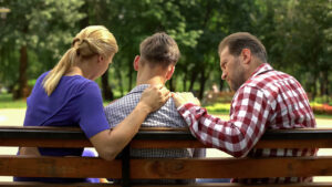 A teen sits between their concerned parents on a park bench. Contact a teen therapist in Phoenix, AZ to learn more about the benefits of counseling for teens in Arcadia, AZ. They can offer counseling for teens in Phoenix, AZ and across the state.