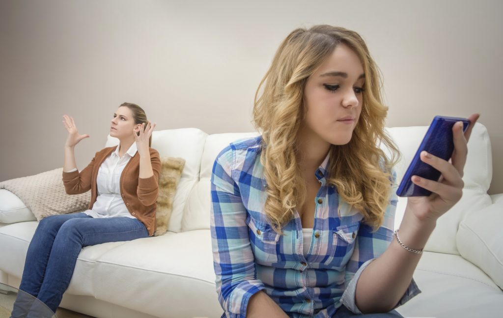 A teen looks at her phone while a parent tries to get their attention. This could represent behavior issues a teen therapist in Phoenix, AZ can address. Learn more about counseling for teens in Phoenix, AZ and counseling for teens in Arcadia, AZ today.