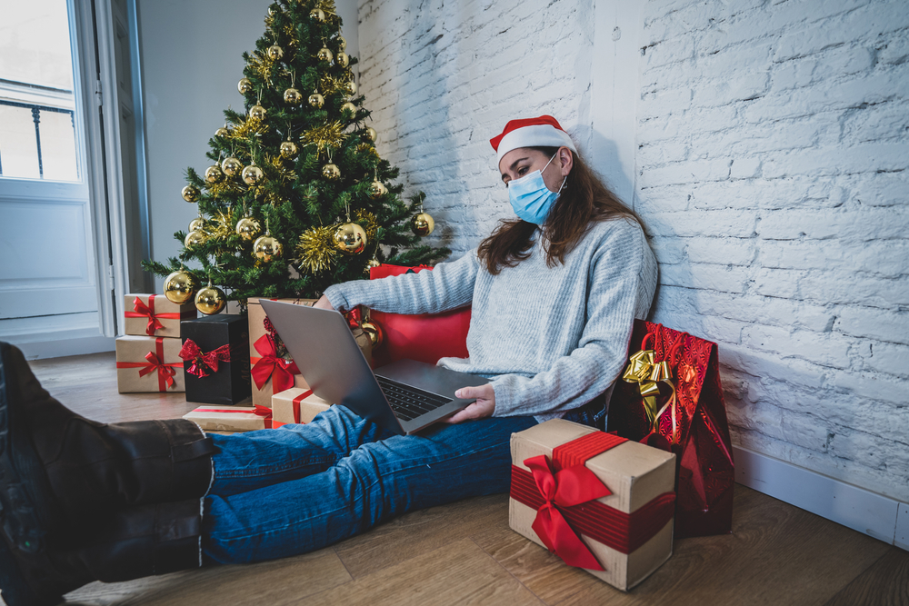 A person sits against a wall next to a christmas tree and gifts while on their laptop. Learn how grieving counseling in Phoenix, AZ can help you during the holiday season. Counseling in Scottsdale AZ can offer support by searching "counseling in Scottsdale AZ".