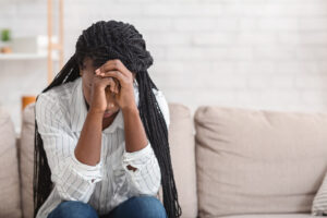 A woman hangs her head while sitting on a sofa. Trauma therapy in Arcadia, AZ can offer support in overcoming PTSD. Learn more about trauma therapy Phoenix by searching “PTSD treatment Scottsdale” today.