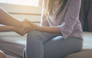 A person holds the hands of a woman sitting on a bed. This support represents the support an anxiety therapist in Arcadia, AZ can offer. Learn more about anxiety treatment in Biltmore, AZ by contacting a therapist in Arcadia, AZ today. We offer online anxiety treatment in Arcadia, AZ and more!