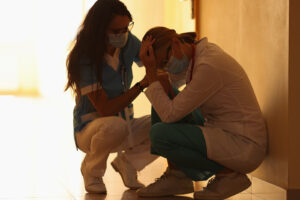 A nurse wearing a mask struggles as someone comforts her. This could symbolize the support a grief counselor in Phoenix, AZ can address. Learn how grief counseling in Phoenix, AZ can offer support by contacting a therapist in Phoenix, AZ today. 