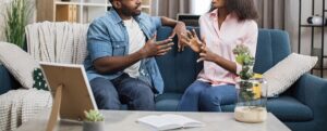 A couple argue with one another while sitting on a couch. Learn how couples therapy in Phoenix, AZ can offer support by contacting a couples therapist in Scottsdale, AZ or therapist in Phoenix, AZ today.