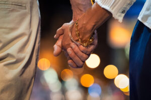 A close up of a couple holding hands against night city lights. This could represent the bonds cultivated via couples therapy in Phoenix, AZ. Learn more about couples therapy in Scottsdale, AZ, and other services.